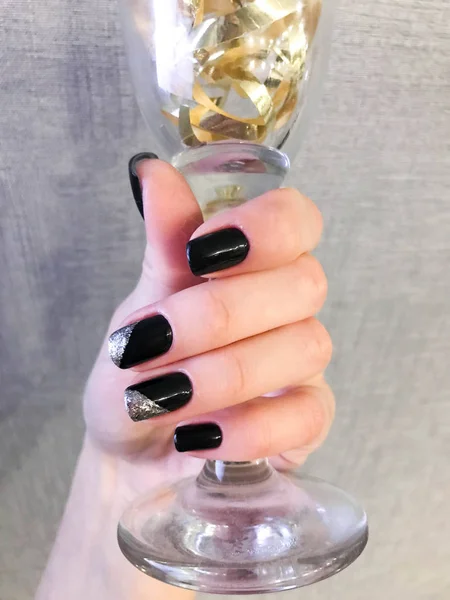 Hermosa mano femenina con dedos delgados y manicura negra con barniz de gel con destellos de plata en las uñas sosteniendo una copa de vino —  Fotos de Stock