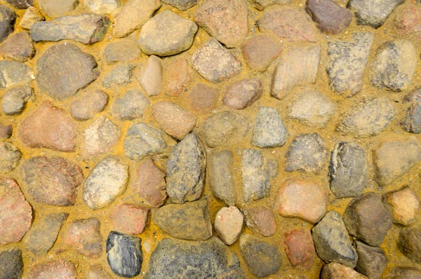 The texture of the stone road, pavement, walls of large gray old medieval round strong stones, cobblestones. The background