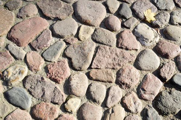 The texture of the stone road, pavement, walls of large gray old medieval round strong stones, cobblestones. The background