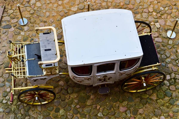 Beautiful white carved wooden royal rich carriage with large wheels decorated with gold patterns next to the old European medieval stone castle and palace — Stock Photo, Image