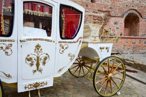 Hermoso carruaje rico real de madera tallada blanca con grandes ruedas decoradas con patrones de oro junto al antiguo castillo y palacio de piedra medieval europeo — Foto de Stock