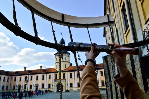 The girl, the woman looks in an old ancient telescope on the European medieval tourist building, the castle, the palace with a spire and a tower on the square