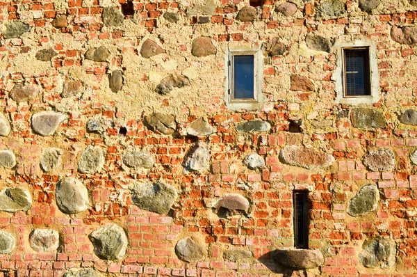 Textura com pequenas janelas estreitas em uma antiga pedra antiga rachada parede de tijolo dilapidado de tijolo vermelho com grandes pedras. O fundo — Fotografia de Stock