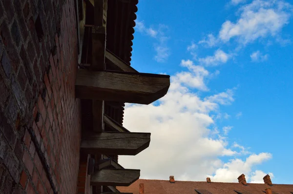 Antigua pared de ladrillo rojo y techo de baldosas de un castillo medieval contra el cielo azul con nubes blancas. El trasfondo — Foto de Stock