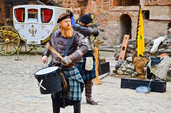 En skotsk krigare, soldat, musiker med ett rött skägg i traditionell dräkt med kjol slår trumman på torget av en medeltida gamla slott. Njasvizj, Vitryssland, 12 oktober 2018 — Stockfoto