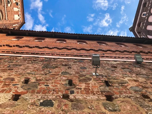 Antigua pared de ladrillo rojo y techo de baldosas de un castillo medieval contra el cielo azul con nubes blancas. El trasfondo — Foto de Stock