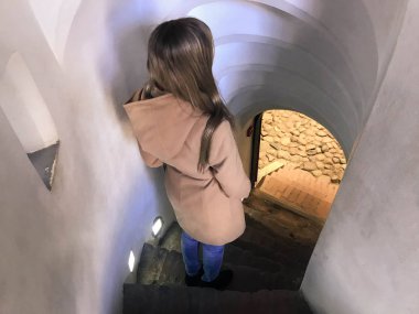 Bir kız, bir kadın dar merdivenlerden aşağı gidiş dik taş sarmal merdiven iner.