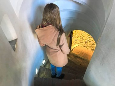 Bir kız, bir kadın dar merdivenlerden aşağı gidiş dik taş sarmal merdiven iner.