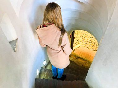 Bir kız, bir kadın dar merdivenlerden aşağı gidiş dik taş sarmal merdiven iner.