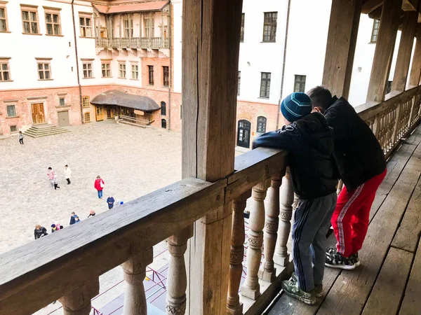 Niños pequeños, niños de pie en un viejo balcón de madera y mirar a la plaza de la ciudad, inclinados sobre la barandilla —  Fotos de Stock