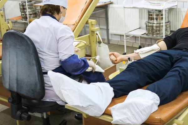 A woman doctor in a white coat takes blood from a donor male lying on a couch in a medical facility Stock Photo