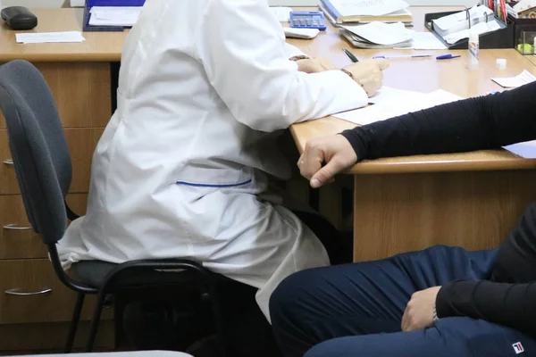 Doctor, medical worker in a white coat advises the patient of a sick man sitting on a chair in a medical institution