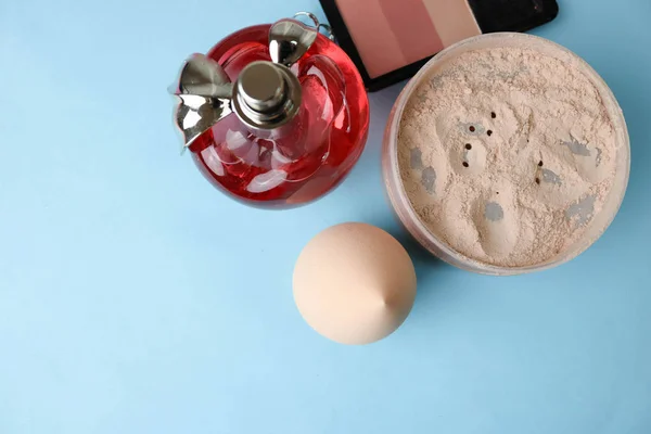 Beauty box, loose matte mineral powder and blush with a beauty blender for makeup and red glass bottle of perfume on a blue background. Flat lay. Top view