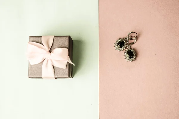 Beauty box, slavnostní krásné dárkové krabičce s mašlí s stříbrné náušnice s drahými kameny na růžové fialové a modré pozadí. Byt leží. Pohled shora — Stock fotografie