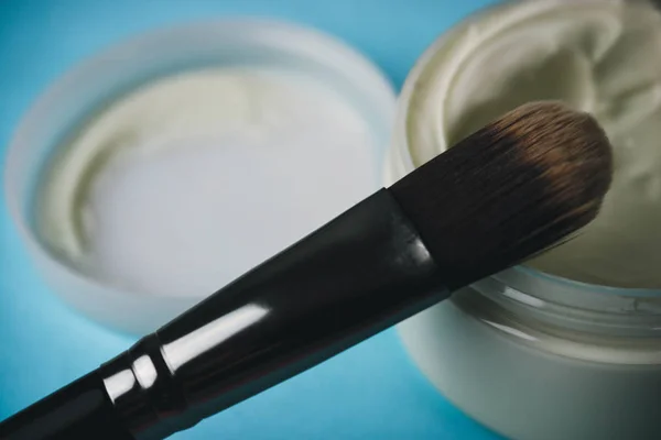 A beauty box with a wooden brush made from natural hard lint for a tone and a round jar of cream, a make-up base with a second skin effect on a blue background. Flat lay. Top view