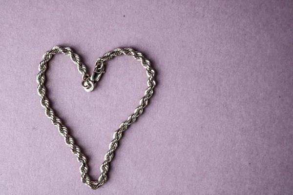 Texture of a beautiful golden festive chain unique weaving in the shape of a heart on a pink purple background and copy space. Concept: love, marriage proposal, marriage, St. Valentine's Day — Stock Photo, Image