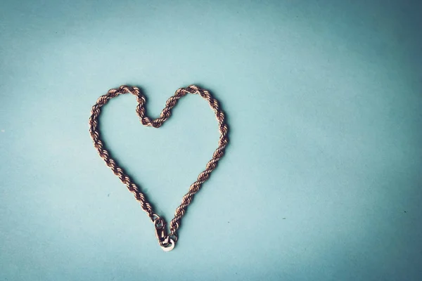 Texture of a beautiful golden dear festive chain of unique weaving in the shape of a heart on a blue background and copy space. Concept: love, marriage proposal, marriage, St. Valentine's Day — Stock Photo, Image