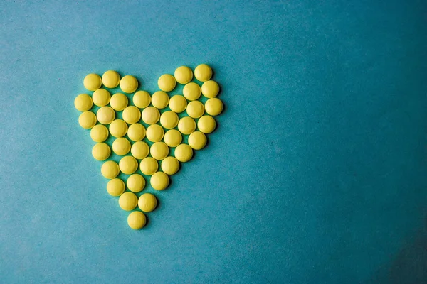 小さな医療 pharmaceptic 黄色の錠剤、ビタミン、薬、青の背景、テクスチャにハートの形で抗生物質をラウンドします。コンセプト: 医学、医療、心臓病。フラット横たわっていた、トップ ビュー — ストック写真