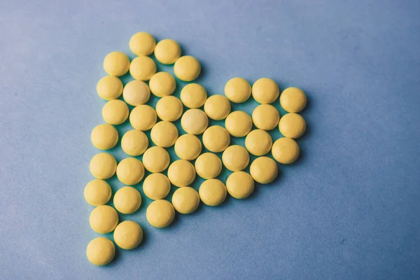 Небольшие медицинские фармацептические круглые желтые таблетки, витамины, лекарства, антибиотики в виде сердца на синем фоне, текстура. Концепция: медицина, здравоохранение, болезни сердца. Плоский, вид сверху — стоковое фото