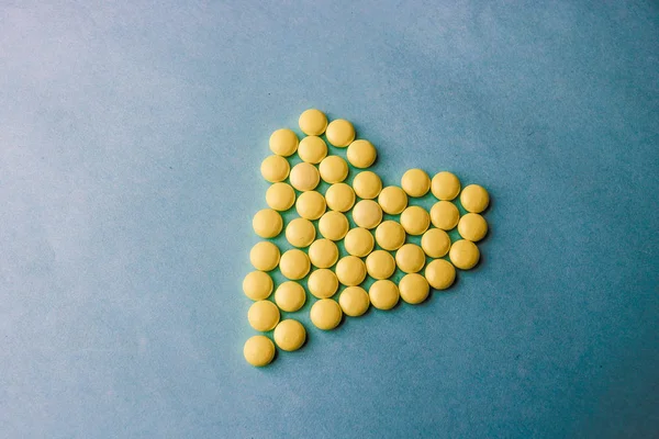 小药用圆形黄色药丸, 维生素, 药物, 抗生素的形式心脏上的蓝色背景, 纹理。理念: 医药、保健、心脏病。平面布局, 顶部视图 — 图库照片