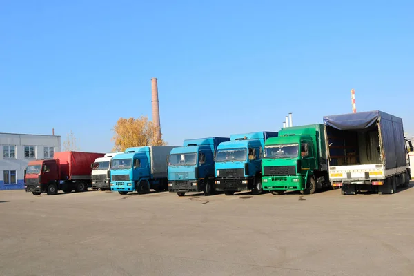 Large heavy cargo trucks with cabs and trailers stand in a row ready for delivery of cargo at the industrial refinery against the background of pipes, transport logistics shop