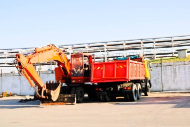 Bir büyük ağır sarı turuncu kamyon bir römork, damperli kamyon ve bir ekskavatör bir kepçe ile bir inşaat sahasında üst üste park etmiş