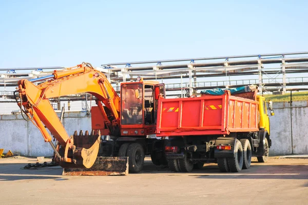 Een grote zware geel oranje vrachtwagen met een aanhangwagen, een kipper en een graafmachine met een pollepel worden geparkeerd in een rij op een bouwplaats — Stockfoto