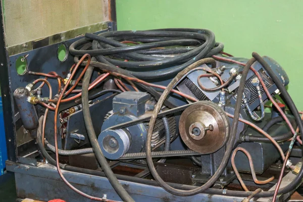 Motor elétrico assíncrono antigo com tubos e mangueiras, acionado por correia numa instalação industrial — Fotografia de Stock
