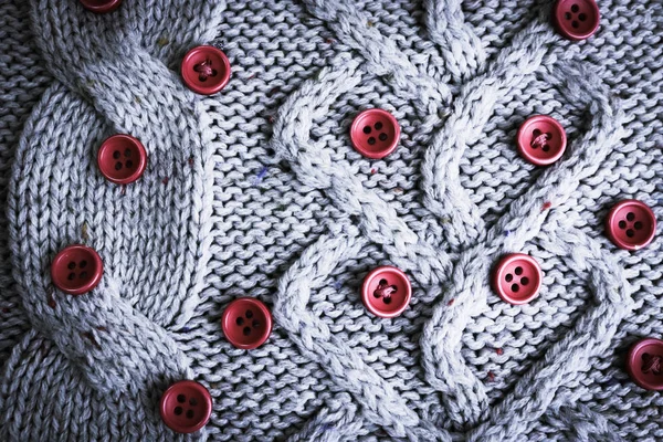 Beautiful texture of a soft warm natural sweater with a knitted pattern of yarn and red small round buttons for sewing. The background — Stock Photo, Image