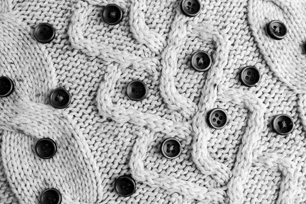Bella texture di un morbido maglione naturale caldo con un motivo a maglia di filati e piccoli bottoni rotondi in bianco e nero. Lo sfondo — Foto Stock