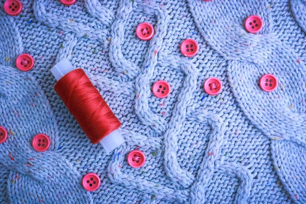 Beautiful texture of a soft warm natural sweater, fabrics with a knitted pattern of yarn and red small round buttons for sewing and a skein of red thread. The background — Stock Photo, Image