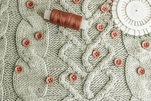 Beautiful texture of a soft warm natural sweater, knitted fabrics and red small round buttons for sewing and a skein of thread, needle bed. Flat lay. The background — Stock Photo, Image