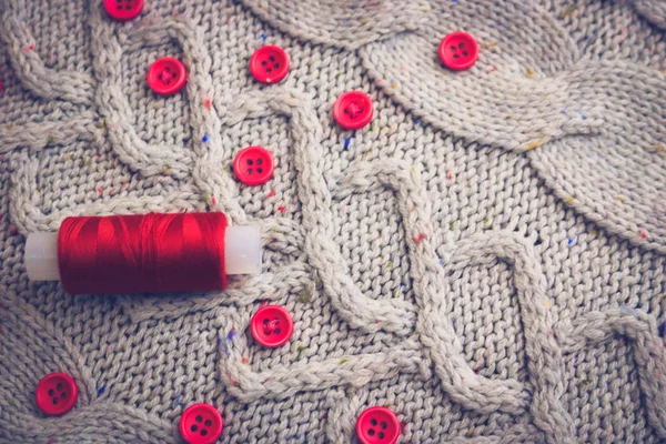 Beautiful texture of a soft warm natural sweater, fabrics with a knitted pattern of yarn and red small round buttons for sewing and a skein of red thread. The background — Stock Photo, Image