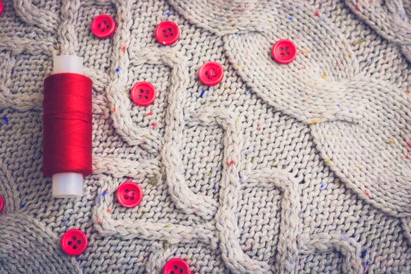 Beautiful texture of a soft warm natural sweater, fabrics with a knitted pattern of yarn and red small round buttons for sewing and a skein of red thread. The background — Stock Photo, Image