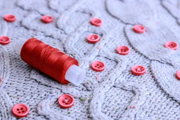 Beautiful texture of a soft warm natural sweater, fabrics with a knitted pattern of yarn and red small round buttons for sewing and a skein of red thread. The background — Stock Photo, Image