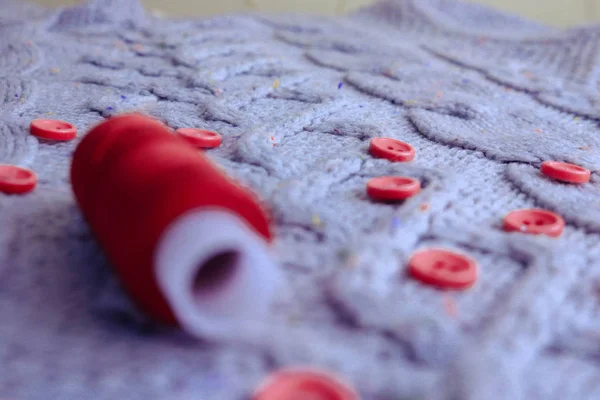 Beautiful texture of a soft warm natural sweater, fabrics with a knitted pattern of yarn and red small round buttons for sewing and a skein of red thread. The background — Stock Photo, Image