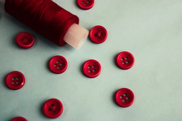 Schöne Textur mit vielen runden roten Knöpfen zum Nähen, Handarbeiten und einer Garnspule. Kopierraum. flach lag. blauer Hintergrund — Stockfoto