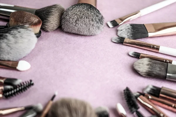 A frame from a set of beautiful different soft makeup brushes from natural lint for targeting beauty and applying a tonal base in a stand and copy space on a pink, purple background