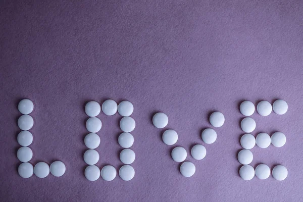 Bela inscrição amor feito de pílulas médicas redondas lisas brancas, vitaminas, antibióticos e espaço de cópia em um fundo rosa púrpura brilhante. Depósito plano — Fotografia de Stock