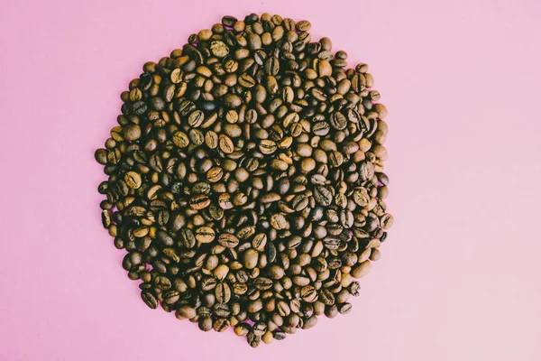 Beautiful round texture of freshly roasted selected delicious rich brown natural fragrant coffee tree grains, Arabica coffee beans, Robusta. Flat lay and copy space on pink purple background