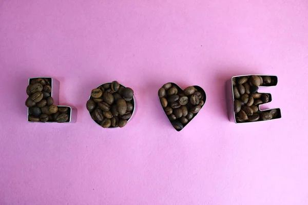 Schöne Textur mit dem Wort Liebe zum Valentinstag Inschrift aus gerösteten ausgewählten braunen natürlichen aromatischen Arabica-Kaffeebohnen, robusta Kopierraum, flache Lage, rosa lila Hintergrund — Stockfoto