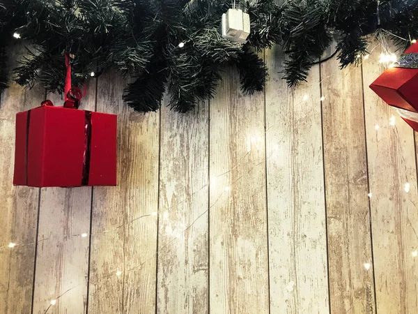 Piccole scatole regalo di festa rosse carine, Natale, decorazione di Capodanno sullo sfondo di rami verdi di albero di Natale con aghi e ghirlande luminose su tavole verticali in legno con cuciture — Foto Stock