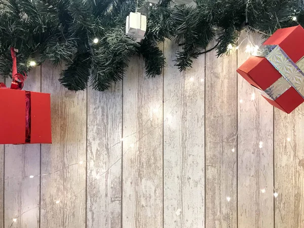 Kleine schattige rode feestelijke cadeau dozen, Kerstmis, nieuw jaar decoratie op de achtergrond van de groene kerstboom takken met naalden en gloeiende slingers op houten verticale planken met naden — Stockfoto