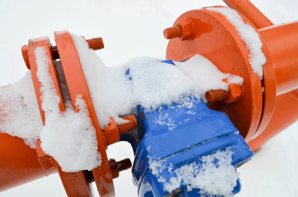 Industrial shut-off regulating protective pipe fittings. Black valve for opening, closing on an iron orange metal pipe with flanges, studs, nuts against the background of white snow in winter