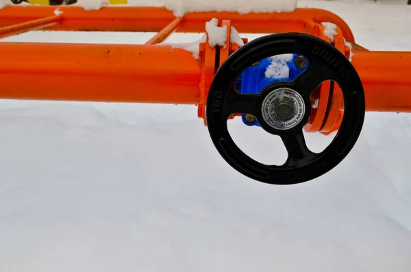 Desligamento industrial que regula acessórios para tubos de proteção. Válvula preta para abertura, fechando em um tubo de metal laranja ferro com flanges, pregos, nozes contra o fundo da neve branca no inverno — Fotografia de Stock