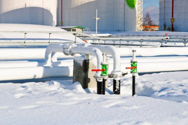 Large white iron metal industrial tanks for storage of fuel, gasoline and diesel and pipeline with valves and flanges at the refinery in the winter
