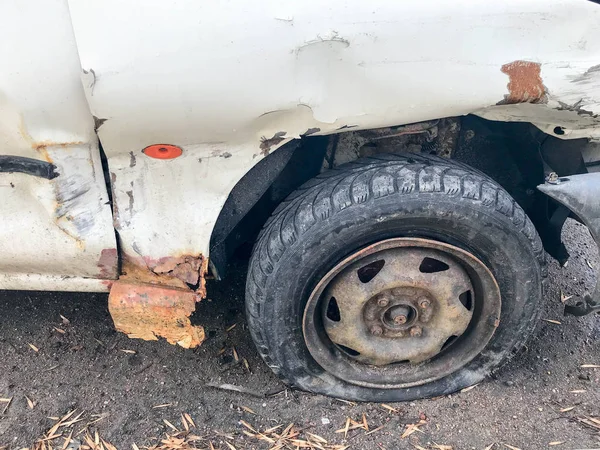 Old white rusty broken car of the carcass with lowered punctured wheels with scratches corrosion and a torn-off bumper with dents and scratches thrown on the road. Auto junk — Stock Photo, Image