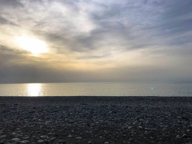 Turuncu gökyüzüne karşı yuvarlak taşlar ve su ile tropikal sıcak bir tatil kayalık plajda deniz, nehir, göl, göl, gölet, güzel sarı parlak gün batımı