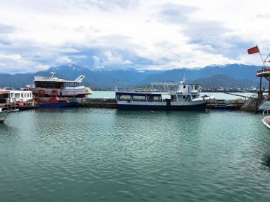 Birçok gemi, tekne, limanda yolcu gemisi ve tropikal denizde su. Sıcak yaz tatili. Mavi gökyüzüne ve yüksek dağlara karşı palmiye ağaçları.
