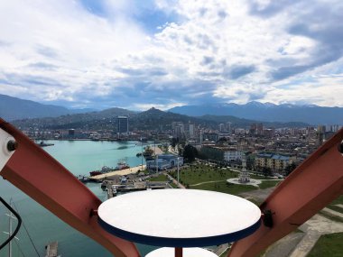 Tropik sıcak bir yazlık tatil beldesinde evler, binalar, mavi deniz ve yüksek dağlar ile şehir üzerinde bir dönme dolap kabin üst görünümü